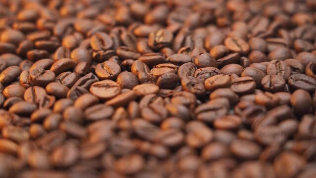 Roasted coffee beans rotate clockwise, warm golden light illuminates the roasted coffee beans. Soft focus