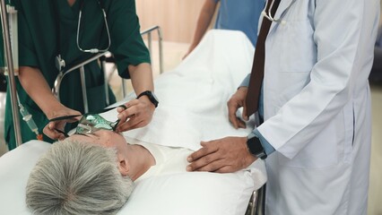 Doctor in protective equipment puts on oxygen mask to connect elderly woman patient lying in bed at hospital, anesthesiologist with mask, Patient in scrub cap with mask ventilation