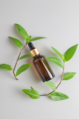 Anti aging serum in a dark glass bottle on a gray background with green leaves. Facial liquid serum with collagen and peptides.