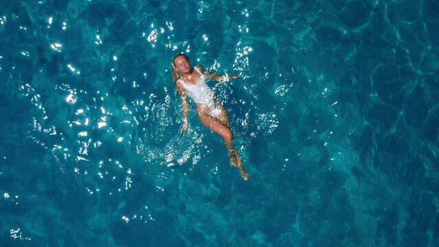 Pretty woman in a white swimsuit swimming in the ocean with clear turquoise water. Vertical drone video from above.