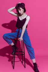 Youth LIfestyle Ideas. One Winsome Relaxed Brunette Girl in Casual Clothing Posing on High Chair With Bunch of Jewelry Over Trendy Pink Background.