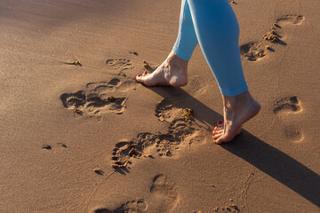 Close up woman legs walking on tropical sunset beach with smooth wave and bokeh sun light wave...