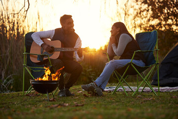 I wrote this for you. Shot of a young man serenading his girl while playing guitar during a camping...