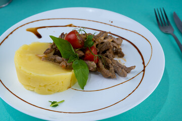 Beef cutlets meatballs with mashed potatoes on a white plate. Meat in sour cream sauce. Tomatoes and basil. Food in the restaurant. Lunch portion. Medallions.