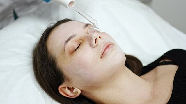 Beautician uses the darsonval device on the client's face. Professional skin care in the salon. The concept of cosmetology and rejuvenation.