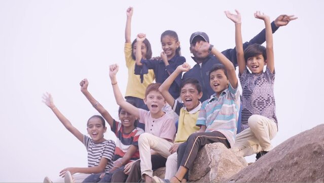 Group of hiking kids shouting with mentor after reaching destination on top of mountian during summer holidays - concept of vacation, holydays and happiness