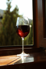 Glass of red wine stands on wooden windowsill