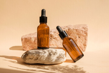 Dark amber glass bottle standing on stone. Natural skin care SPA beauty product design. Mineral organic oil cosmetics on beige background. Mock-Up. Oily pipette. Face and body treatment. Front view