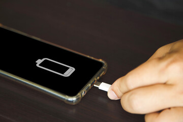 Close up a man hands using a USB tye C cable to charge mobile phone on wooden table