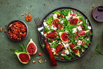 Fototapeta na wymiar Delicious summer salad with figs, feta cheese, walnuts, arugula and sweet jam dressing on rusty green table background, top view, negative space