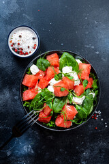 Delicious summer watermelon salad bowl with feta cheese, spinach and pea sprouts on gray table background, top view, negative space