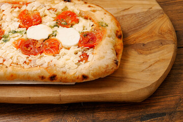 Premium high quality pizza with mozzarella cheese and tomato. Italian style dish with top products on wooden board and table.