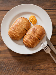 Serving of two ham and cheese pies on a white plate on wooden table. Simple food concept. Pastry product for lunch.