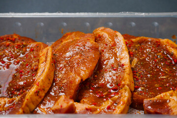 Fresh pork chops in Korean style marinade with spicy sous and herbs. Summer barbeque product in a plastic tray on dark surface. Meat industry. Orient inspired flavor. Close up