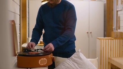 A man puts a record in a gramophone to listen to classical music. A vinyl record of classical music is used in a gramophone player. Put on a record to listen to music