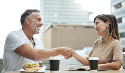 Business meetings made better over lunch. Shot of two businesspeople shaking hands while having lunch outside an office.