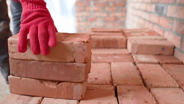 Builder in red gloves neatly stacks red ceramic bricks