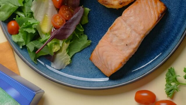 Vertical flat lay video: chef adds olive oil to the dish with baked salmon fillet and vegetable salad