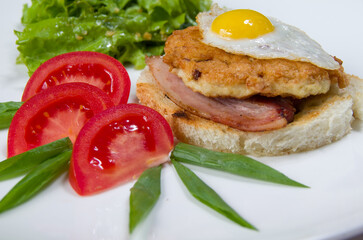 Sandwich with meat and egg, fresh green salad, fresh red tomatoes on a white bowl.
