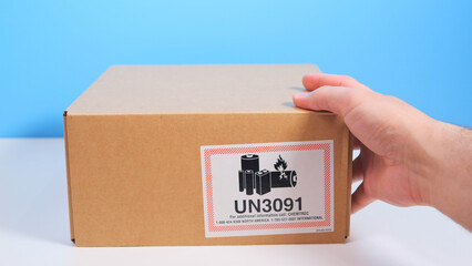 Postman or courier weighs brown box with sign 'UN 3091' on a white industrial scale. Sending a...