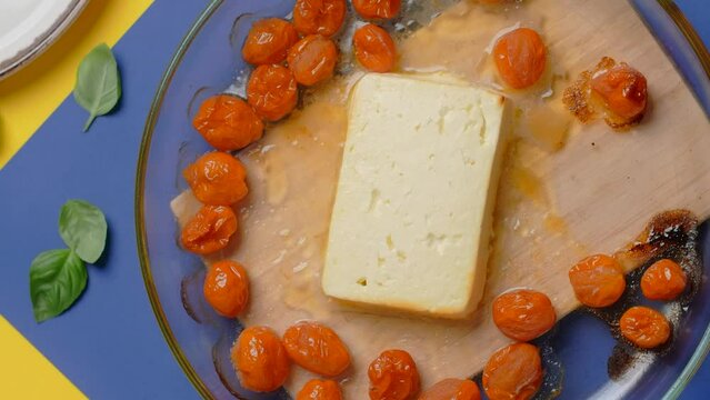 Vertical flat lay video: the cook puts plate with hot baked tomatoes and feta cheese