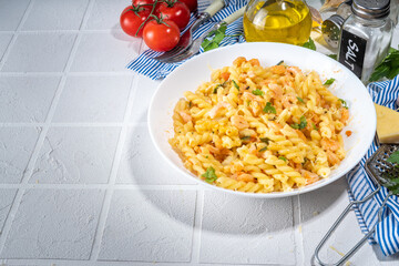 Italian mediterranean lunch concept. Fusilli pasta with seafood, shrimp, vegetables and creamy sauce. On a white tile table, with spices for dinner copy space