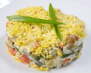Olivier vegetable salad with greens on a white plate.