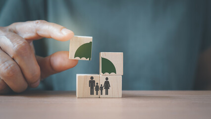 senior's hand complete umbrella over family icon on wooden cube blocks, for life or group insurance