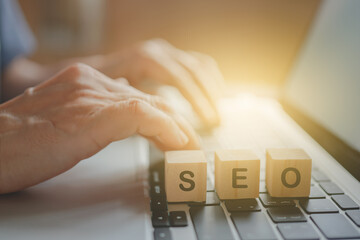 SEO, meaning search engine optimization, on wooden cube block with blurred senior key computer for...