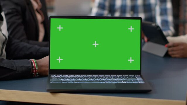 Laptop display with green screen background on office desk, people attending business meeting. Isolated mockup template with blank chroma key and copy space on computer screen. Close up.
