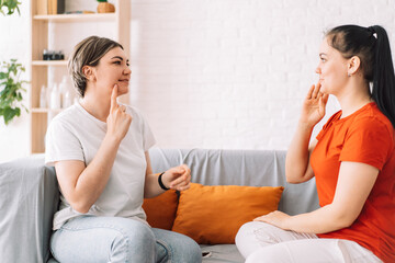 The teacher teaches the girl sign language while sitting on the couch.