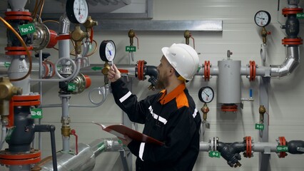A bearded man with blue eyes in overalls and a helmet. The engineer checks the pressure readings in the pipeline using pressure gauges and compares them with the allowable pressure settings.
