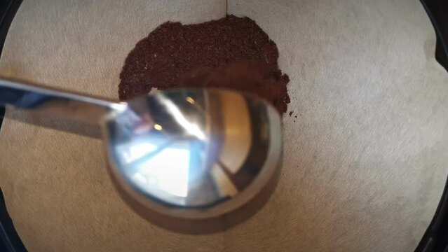 Filling ground coffee in a brown filter with a round, silver spoon. Static close-up footage