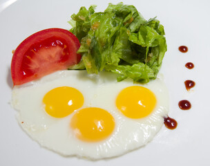 Fried eggs from three eggs and with vegetables on a white background. Lettuce and tomatoes.
