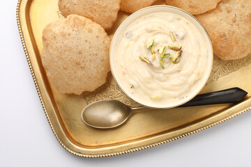Shrikhand & Puri, Shrikhand is an Indian sweet dish made of strained curd,garnished with dry fruits and saffron. Served in a ceramic bowl & brass plate with Puri, Deep fried flat bread.Selective focus