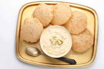 Shrikhand & Puri, Shrikhand is an Indian sweet dish made of strained curd,garnished with dry fruits and saffron. Served in a ceramic bowl & brass plate with Puri, Deep fried flat bread.Selective focus