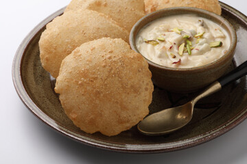 Shrikhand & Puri, Shrikhand is an Indian sweet dish made of strained curd,garnished with dry fruits and saffron. Served in a ceramic bowl & plate with Puri, Deep fried flat bread.Selective focus