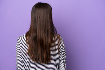 Young Brazilian woman isolated on purple background in back position and looking side