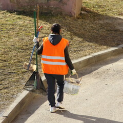 European janitor with broom and yellow uniform walks on sidewalk at Sunny spring day. Municipal...
