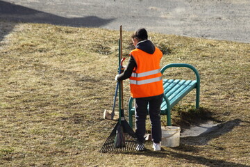 Russian working janitor woman with a broomstick on the grass at spring day