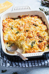 Baked potato gratin with cheese and thyme in oven dish, gray background.