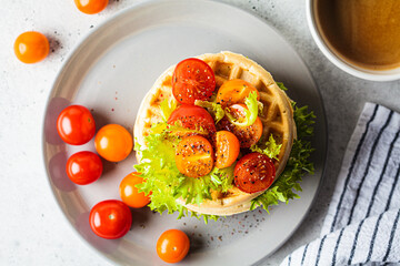 Stack of savory waffles with cherry tomatoes and lettuce, top view, gray background, breakfast concept.