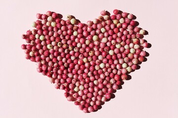 pink pepper berries in the shape of a heart, closeup in the sun , pink background 