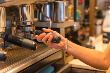 Hands of female coffee shop owner preparing coffee in a coffee machine, preparing a latte