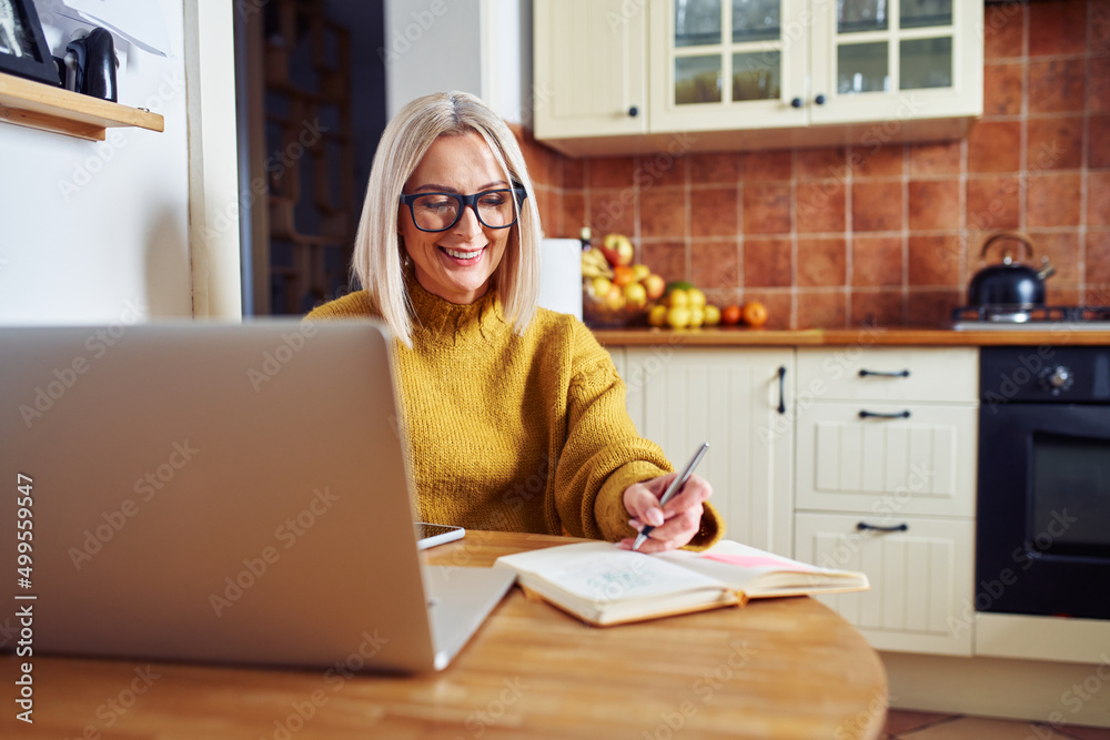 Wall mural Smiling mature woman making notes while calculating home finances