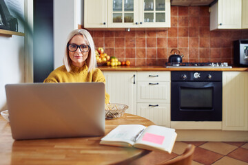 Mature woman using laptop in a kitchen - Powered by Adobe