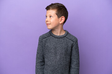 Little boy isolated on purple background looking to the side and smiling