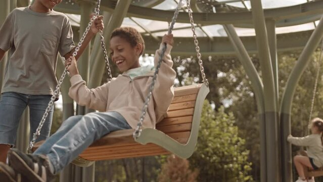 Slowmo of 12 year old African American boy swinging his cute little brother at playground on sunny day