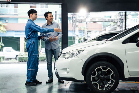 Asian automotive mechanic explain car condition to client in garage.