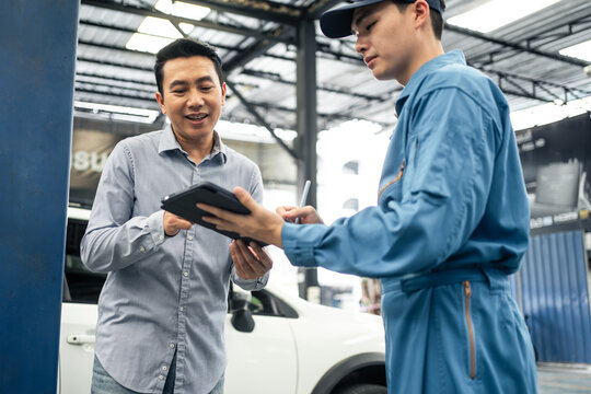 Asian automotive mechanic explain car condition to client in garage.